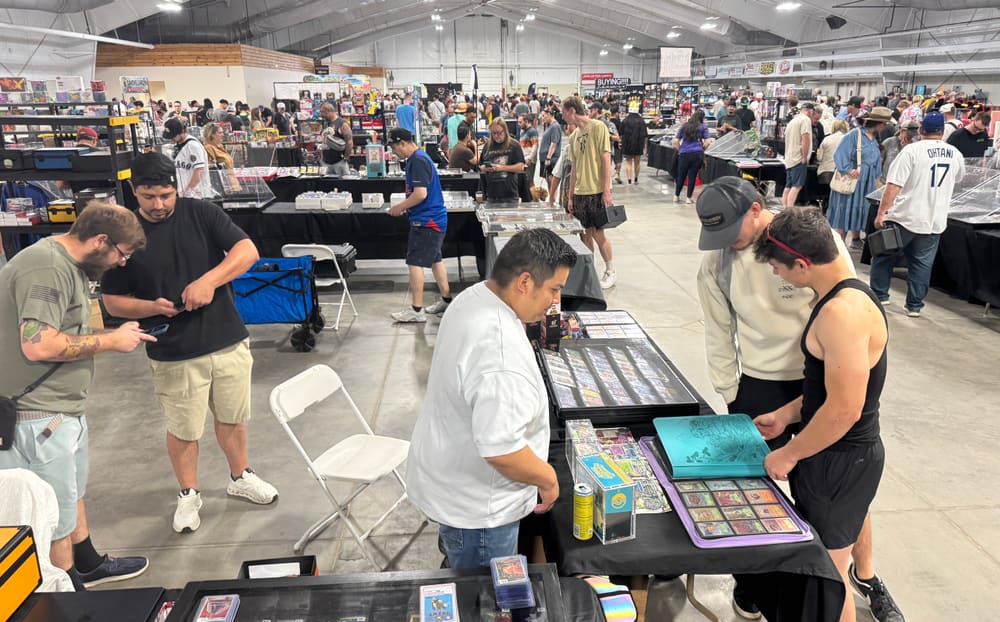A vendor flipping through a binder of cards with two collectors at his table